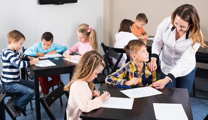 Obraz na płótnie Canvas Positive little boys and girls with teacher drawing in classroom