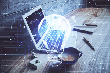 Computer on desktop in office with bulb icon hologram. Double exposure. Concept of idea.