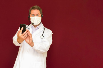 Young caucasian doctor with stethoscope, medical mask talking with patient online red background