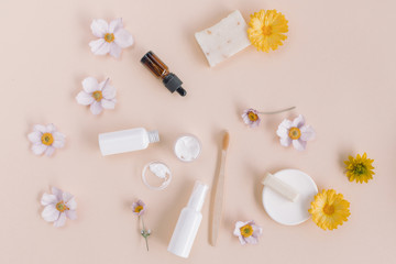 White containers of beauty treatments, aromatherapy oil, organic soaps, eco friendly toothbrush, flower buds on beige background.