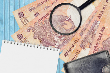 10 Indian rupees bills and magnifying glass with black purse and notepad. Concept of counterfeit...