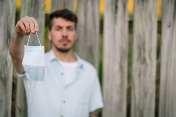 Caucasian man hanging a medical face mask on his hand on an open air environment