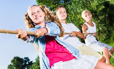 Fototapeta premium Happy cheerful children playing tug of war during joint games outdoors on sunny day
