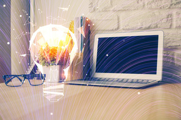 Computer on desktop in office with bulb icon hologram. Double exposure. Concept of idea.