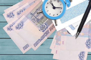 50 russian rubles bills and alarm clock with pen and envelopes. Tax season concept, payment deadline for credit or loan. Financial operations using postal service