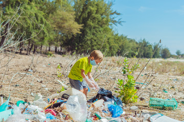 Volunteer boy in face mask helps to pick up garbage which pollute beach near forest. Problem of...