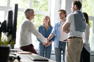 Welcome to our team! Business men in smart casual wear shaking hands while working in the creative office