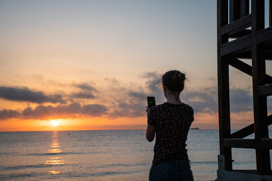 A woman taking pictures with her ohone during sunrise