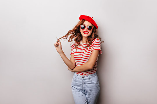Cute caucasian girl in jeans and beret standing on white background. Indoor photo of laughing debonair young woman with ginger hair.