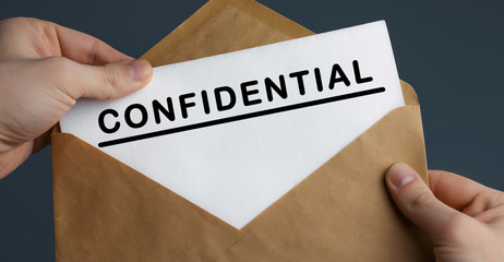 Male hands holding craft envelope with text CONFIDENTIAL on blue background