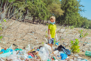 Volunteer boy in face mask helps to pick up garbage which pollute beach near forest. Problem of...