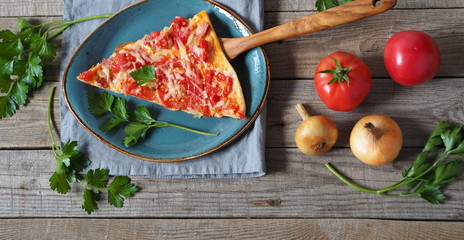 Advertising background with homemade pizza with tomatoes, cheese, sausage.Sprigs of parsley are laid out around the sliced slice of pizza on a plate on a wooden backgroun