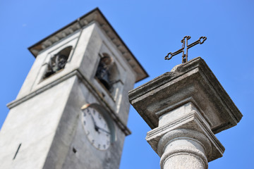 Kirchenkreuz vor blauem Himmel neben Kirchturm mit Uhr