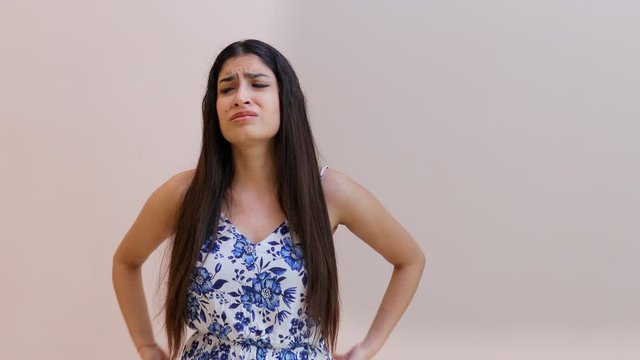 Young girl showing negative emotions while standing against a wall background. Portrait shot of a beautiful Indian female grabbing her head and freaking out in panic - facial expressions concept