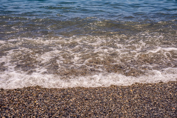 Sea wave reaching a calm beach with sand and pebbles. Front view close-up.