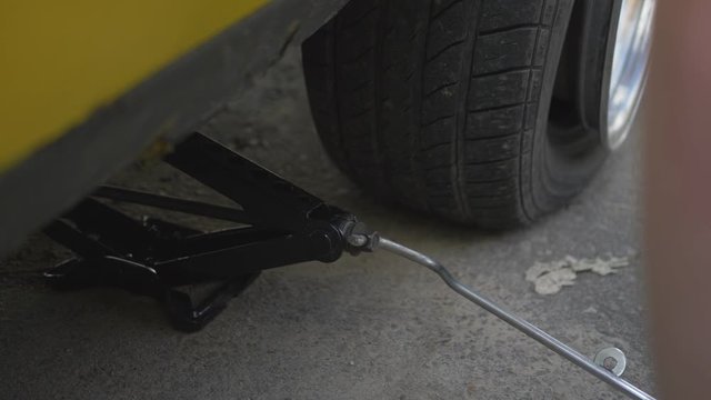A Man With A Lifting Jack Lifts A Yellow Car With A Flat Tire.