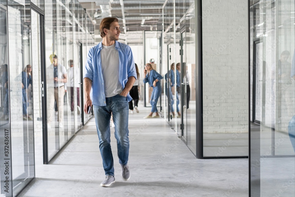 Wall mural On the way to business meeting. Full length of young modern people in smart casual wear having a discussion while walking through the office