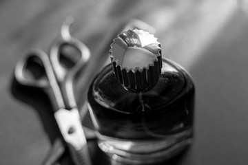 Black and white photo of a bottle with scissors and a comb on a black background.