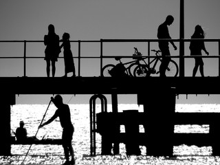 Silhouettes of people on and under a pier