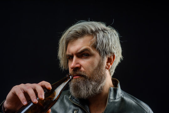 Beard man drinking beer from bottle. Handsome bearded male in leather jacket drinks craft bottled beer. Bearded man holds bottle of beverage.