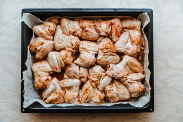 Raw Marinated chicken meat wings in a marinade on a baking sheet.