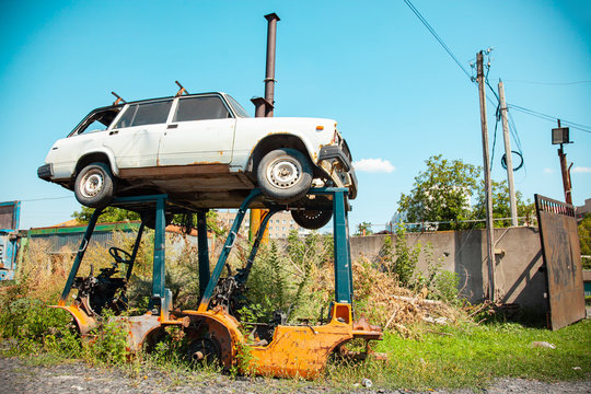 Old rusty car stands on metal supports in a landfill.