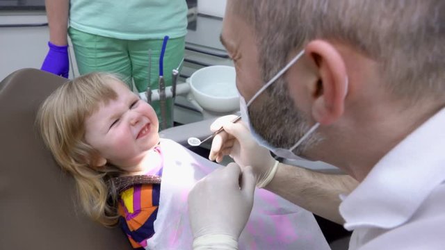 The dentist asks a little girl to open the mouth and show her teeth. The Dental Clinic