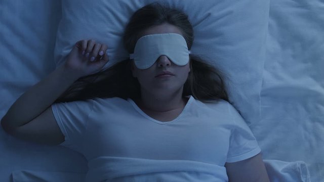 Plus size woman in sleep mask lying in bed, having dreams, enjoying home comfort