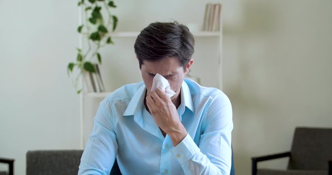 Adult attractive upset businessman feeling stress, crying sobbing, wiping his nose with napkin handkerchief, close up emotions of grief. Office worker male comically funny suffering sitting at table