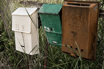 Vintage rustic mailboxes of different colors pinned on a fence.