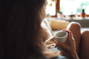 Close up shot of woman holding coffee cup while relaxing in living room at home