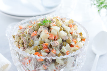 Classic festive salad Olivier in a crystal salad bowl on a white table, horizontal