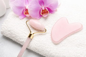 Obraz na płótnie Canvas Rose Quartz jade roller and Gua Sha massager on towel on stone background. Massage tool for facial skin care, SPA beauty treatment concept