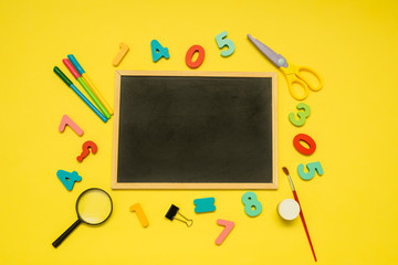 background with an empty slate and school supplies on a yellow background