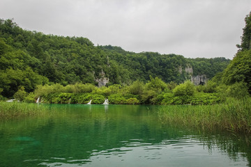 A view of a lake over reeds with a waterfall and mountain in the background