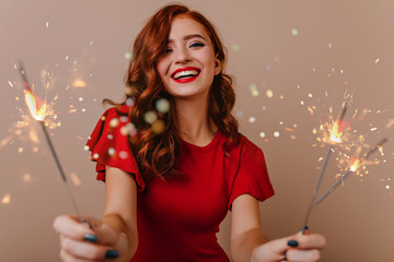 Adorable white woman posing with bengal lights. Gorgeous red-haired girl holding sparklers and...