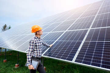 Male engineer in a helmet with a tablet in his hands standing near the solar panels, looking up. Green ecological power energy generation. Solar station development concept. Home construction.