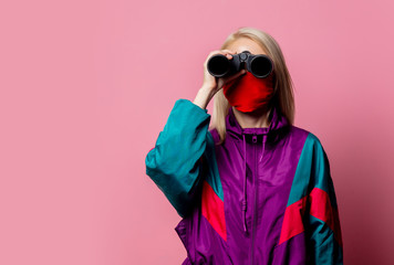 Woman in face mask and 80s clothes with binoculars on pink background