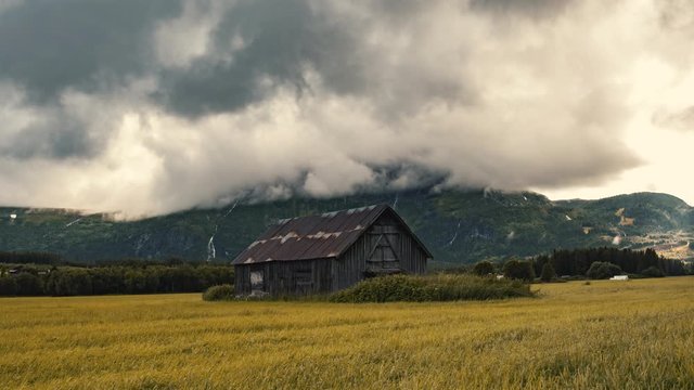 Abandoned Barn House Settled On Autumnal Lush Field With Thick Rolling Clouds Above- Wide Shot