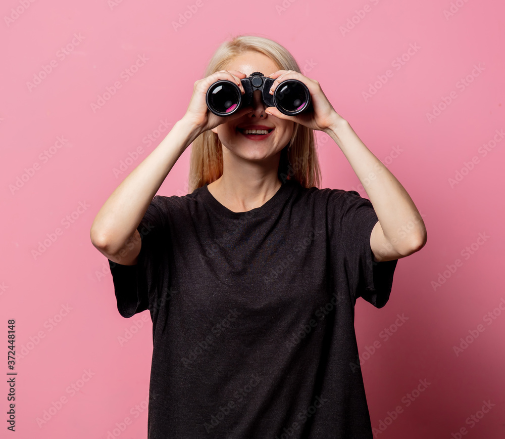 Wall mural woman in black t-shirt with binoculars on pink background