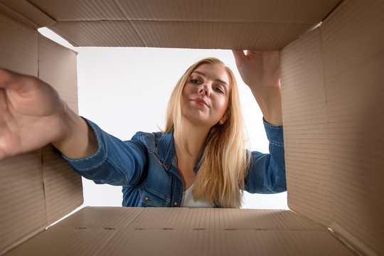 Young beautiful girl blonde, opens and peeks into a cardboard box. To get or to put things to move, bottom view.