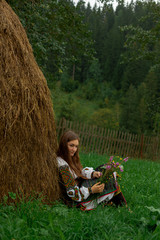 Naklejka na ściany i meble girl with loose hair with a bouquet of wildflowers sits on the grass