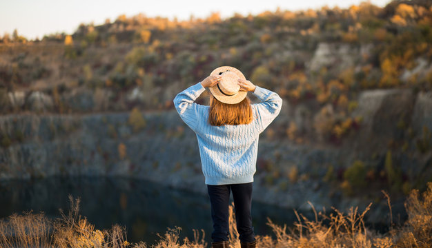 Autumn girl in blue sweater and hat standing backwards and admire nature lake view. Autumn forest colors with girl back view.