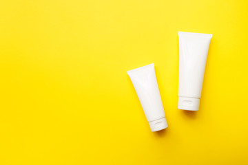 Cream bottles on bright yellow background, top view, copy space. Cosmetics product and skin care concept. Mock up