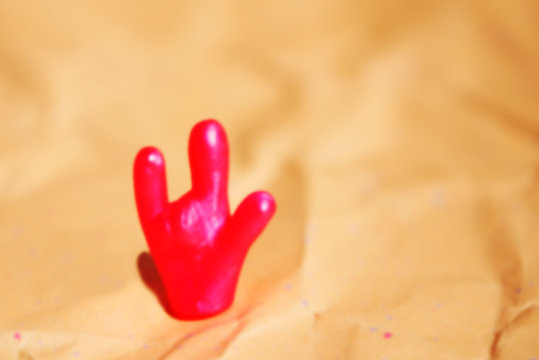 Defocused photo of a bright toy hand with "I love you" gesture.  Space for lettering and design