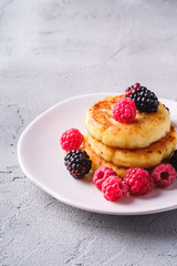 Cottage cheese pancakes, curd fritters dessert with raspberry and blackberry berries in plate on stone concrete background, angle view