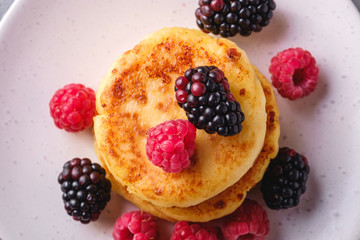Cottage cheese pancakes, curd fritters dessert with raspberry and blackberry berries in plate on stone concrete background, top view macro