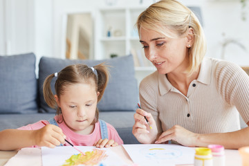 Little girl sitting at the table and painting a picture together with her mother at home