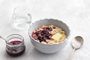 Delicious oatmeal porridge with butter and jam in a gray bowl on a light gray background. healthy homemade breakfast. selective focus, space