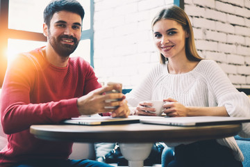 Half length portrait of young good looking friends looking at camera while having recreation time in comfortable sunshine cafe with modern smartphone.Positive colleagues resting during work break